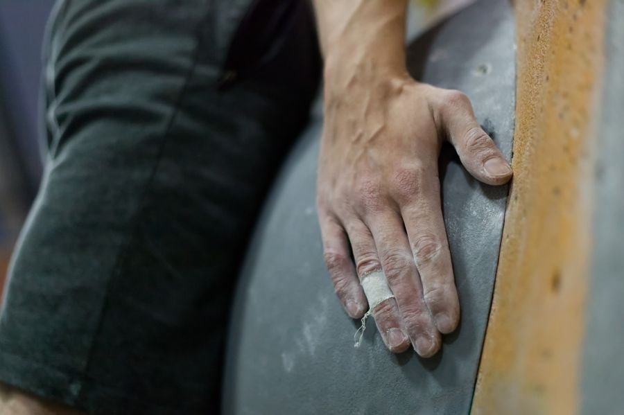 Climber's chalked hand gripping a wall hold — the kind of high-load finger extension that can cause mallet finger