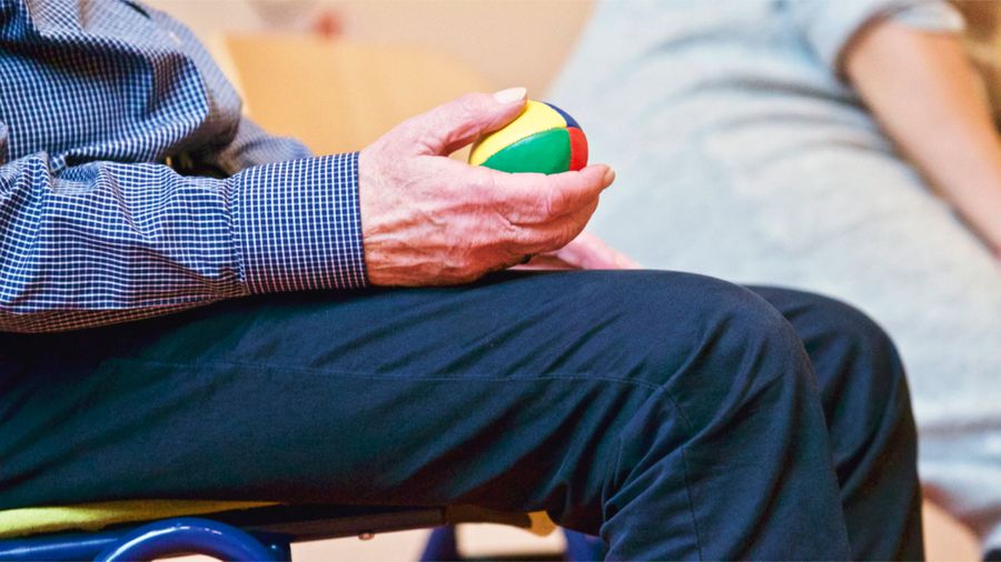 Elderly patient holding a colorful therapy ball during post-surgical hand rehabilitation exercise