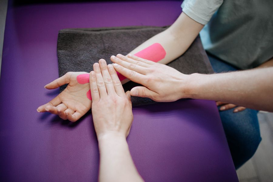 Therapist applying kinesio tape to a patient's forearm and wrist during elbow rehabilitation